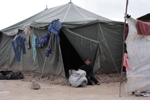 Free Children outside a large tent in a desert refugee camp, evoking resilience and survival. Stock Photo