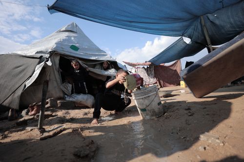 Free A family in a tented shelter performs daily chores amid challenging conditions. Stock Photo