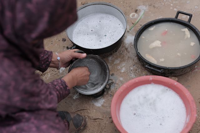 Person washing dishes outdoors with soapy water and multiple containers.