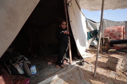 Free A young child stands at a tent entrance in a sunny outdoor refugee camp setting. Stock Photo