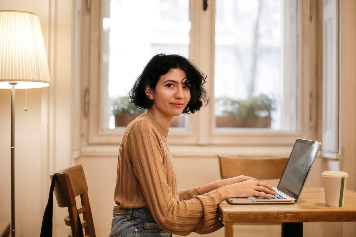 A smiling woman working on a laptop at a wooden table at home