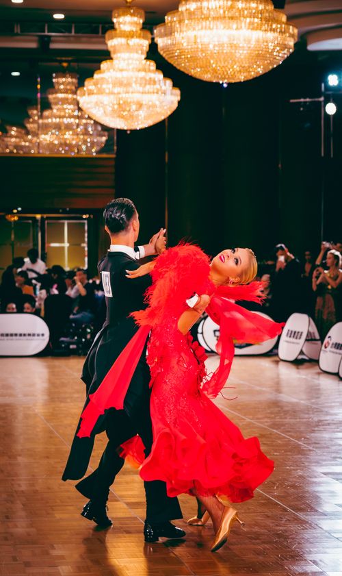 Free Dancers in elegant attire perform a sophisticated ballroom routine under sparkling chandeliers. Stock Photo