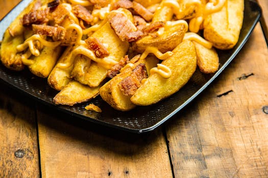 Delicious crispy potato wedges topped with bacon and cheese sauce on a rustic wooden surface.