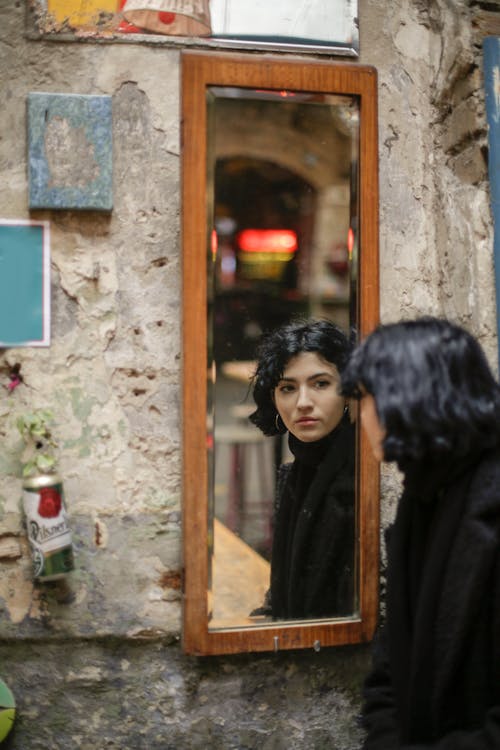 Woman in Black Coat Standing Beside Brown Wooden Framed Glass Window