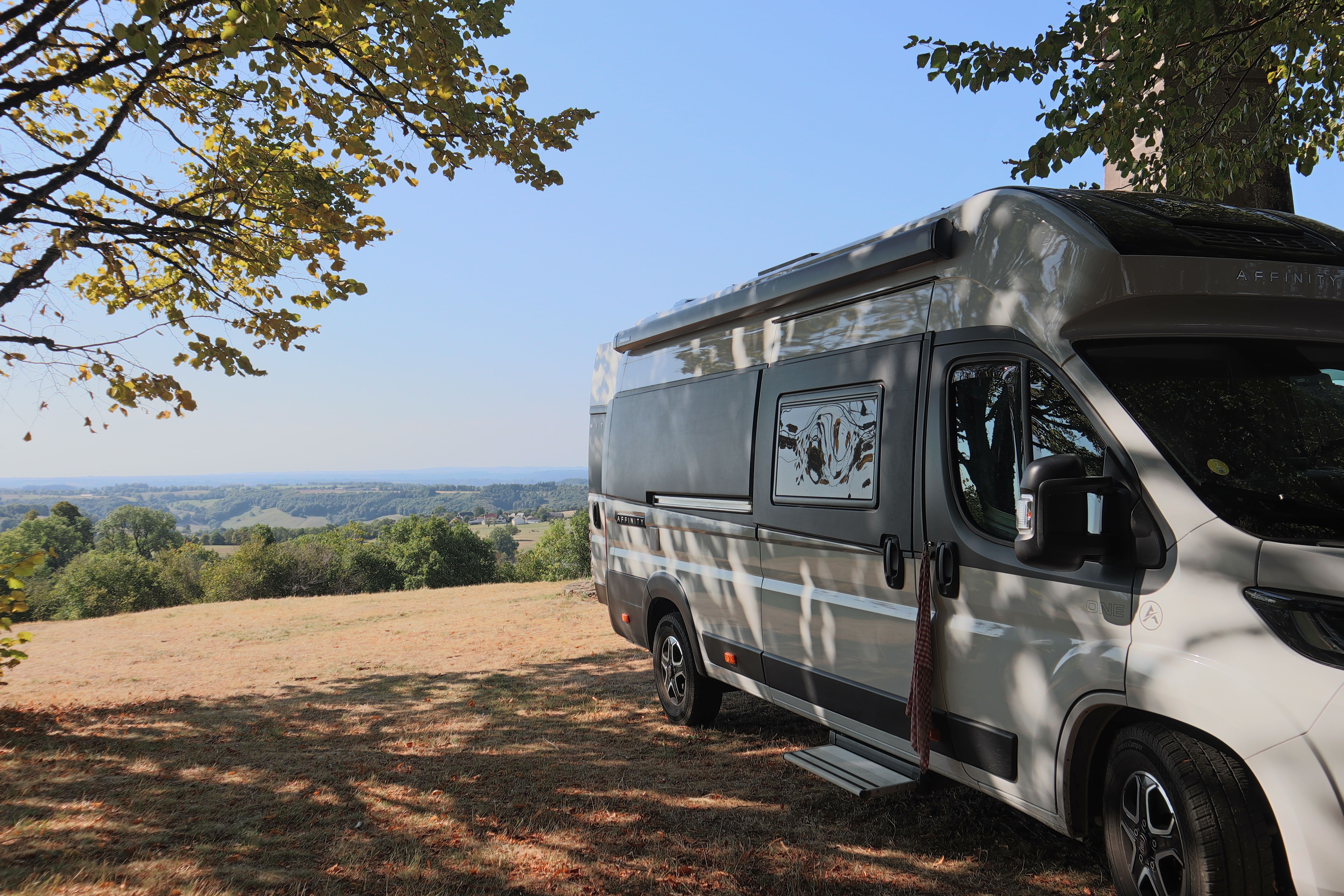 Camping-car garé sous un arbre face à la campagne française