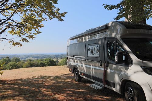 Free Campervan parked under a tree with a scenic view of the French countryside under clear blue skies. Stock Photo