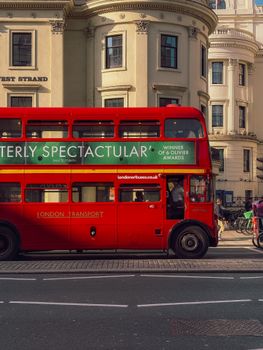 Vibrant red double-decker bus passing classic London architecture in sunlight.