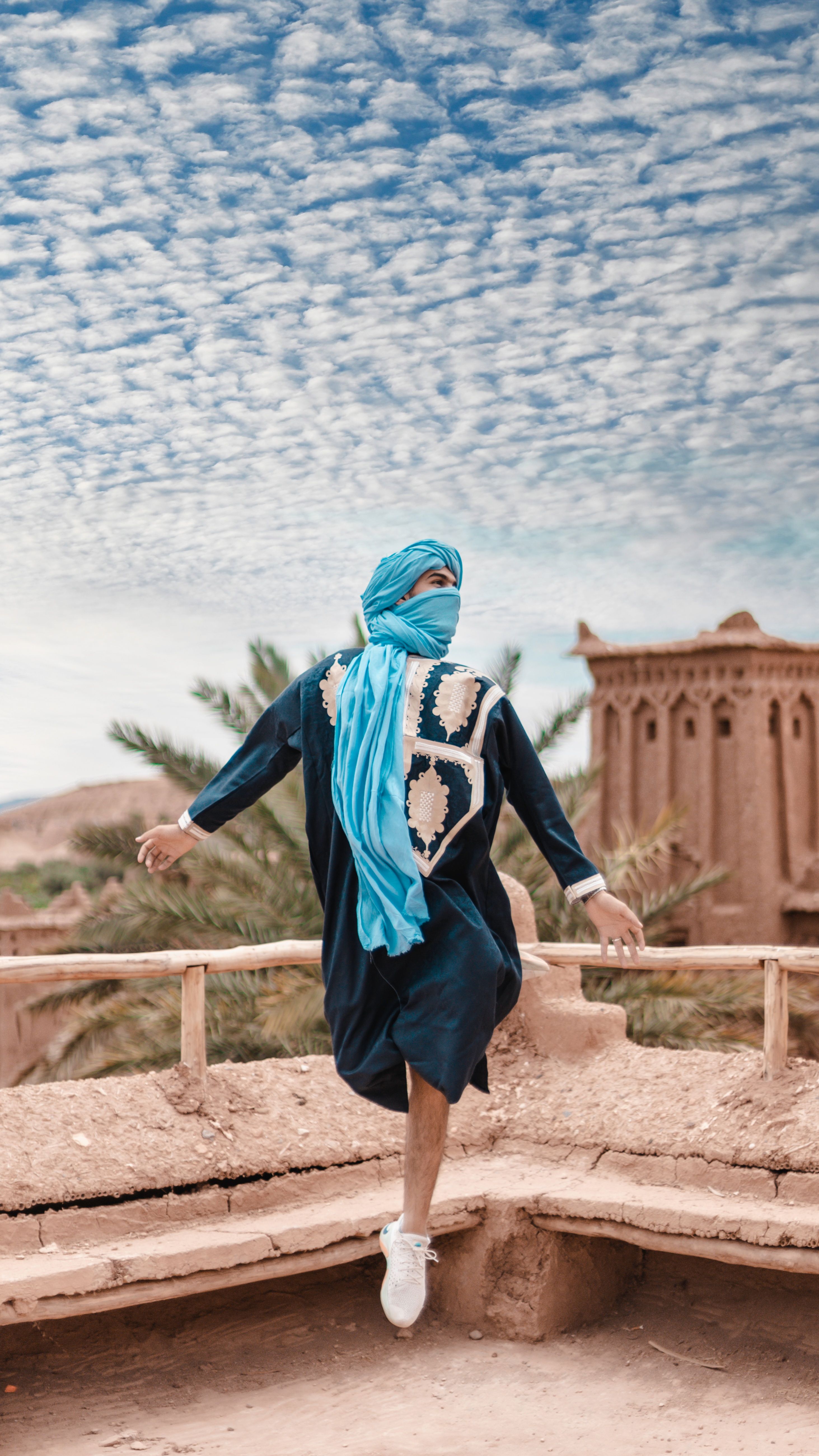 Person in traditional Moroccan clothing against a desert backdrop with a vibrant sky.