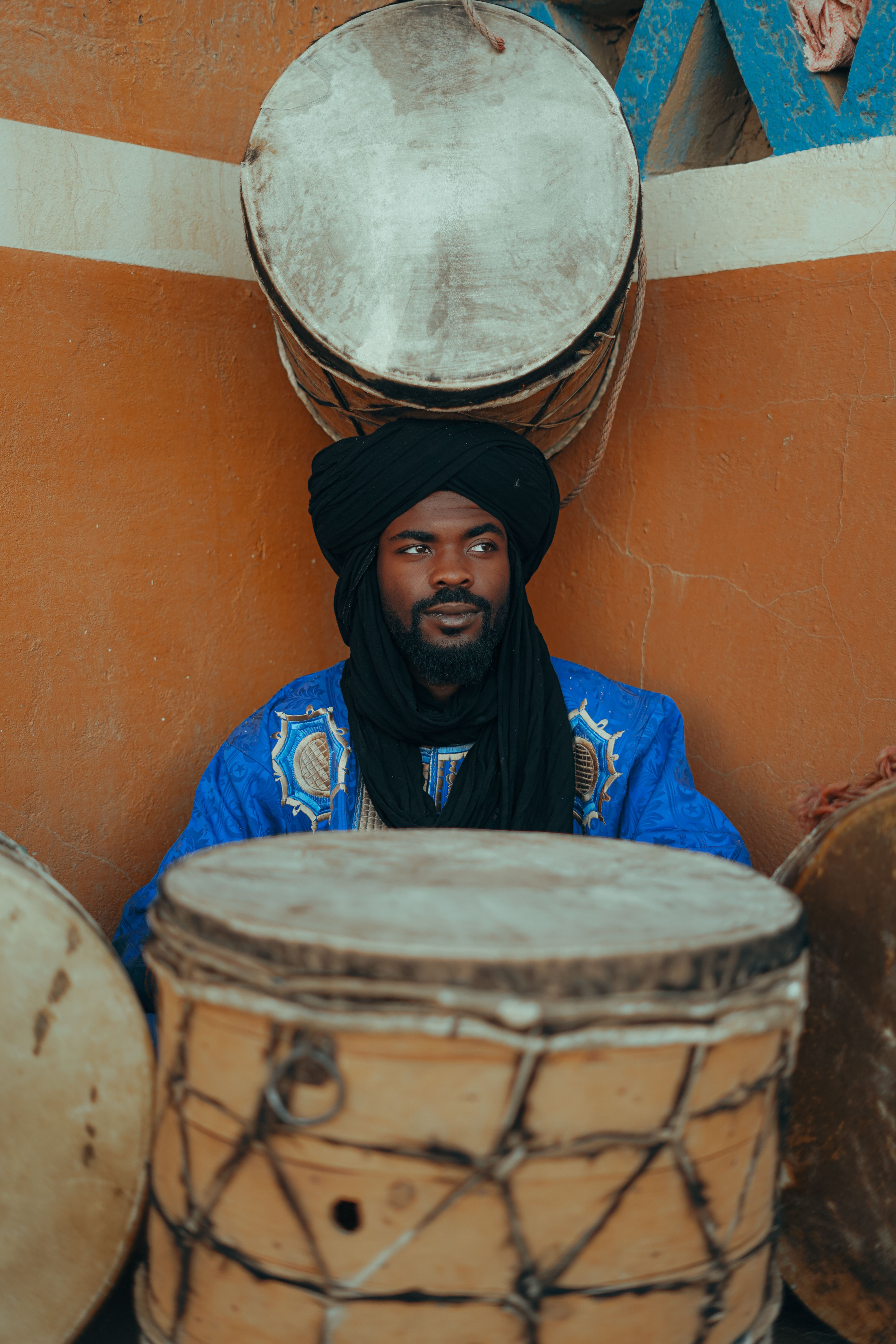 A Moroccan man in vibrant attire surrounded by traditional drums, showcasing cultural music heritage.