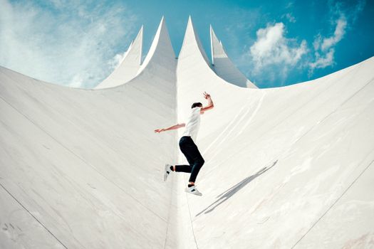 A person in mid-air against a striking modern architectural background under a bright sky.