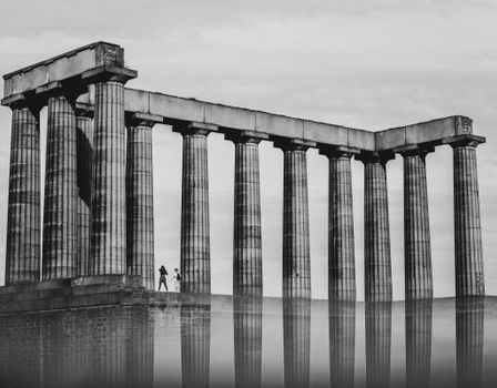 Monochrome image of ancient Roman-style columns with two people walking nearby.