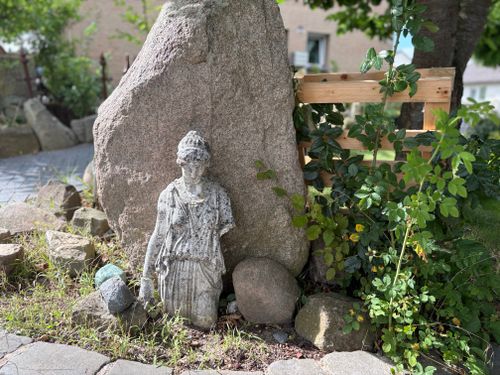 Free Ancient stone statue surrounded by lush greenery in a tranquil outdoor garden. Stock Photo