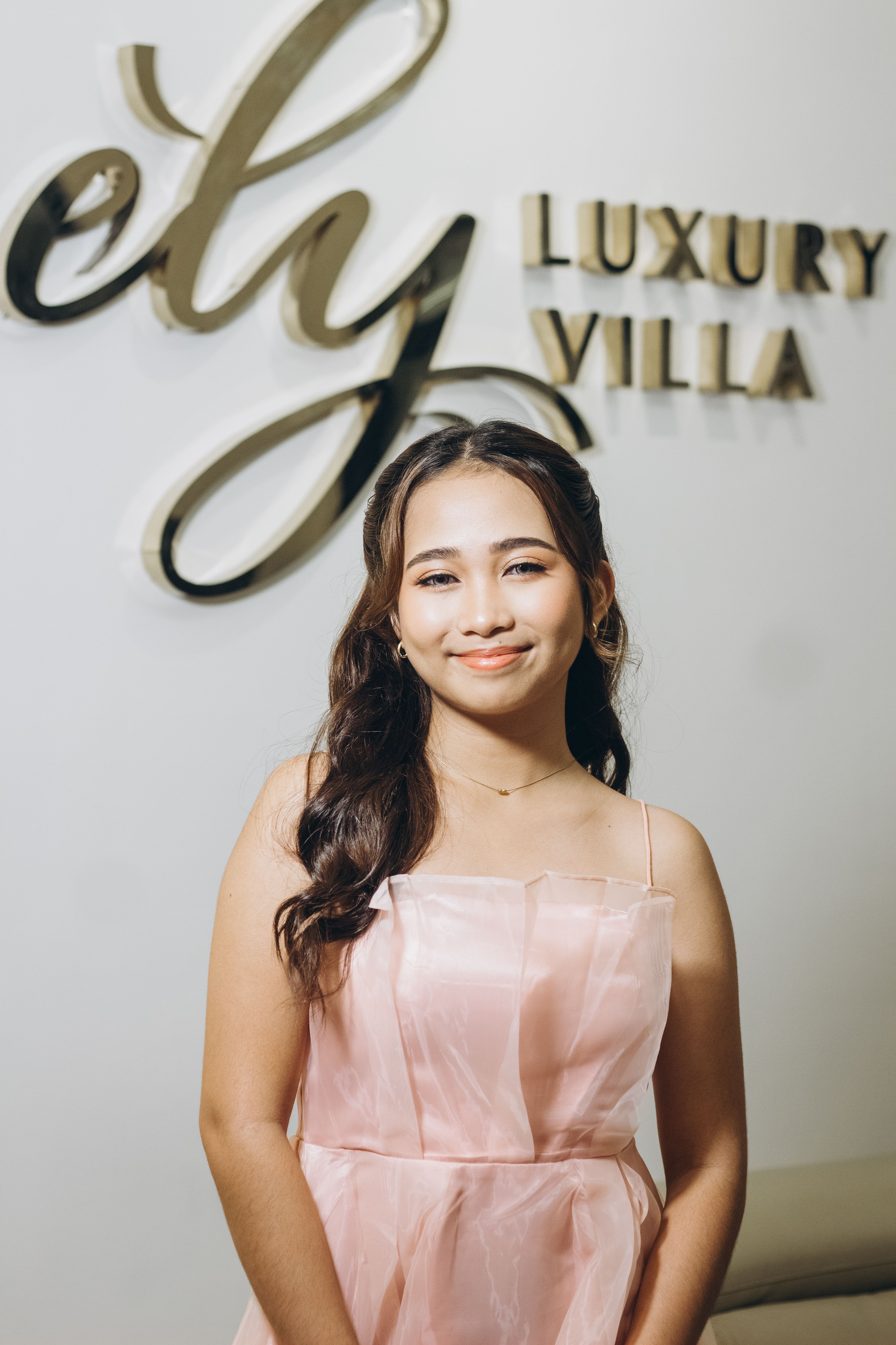 A young woman in a pink dress at a luxury event, smiling confidently indoors.