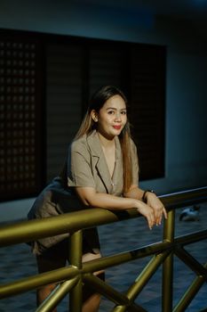 A woman in casual attire leaning on a railing indoors during nighttime.