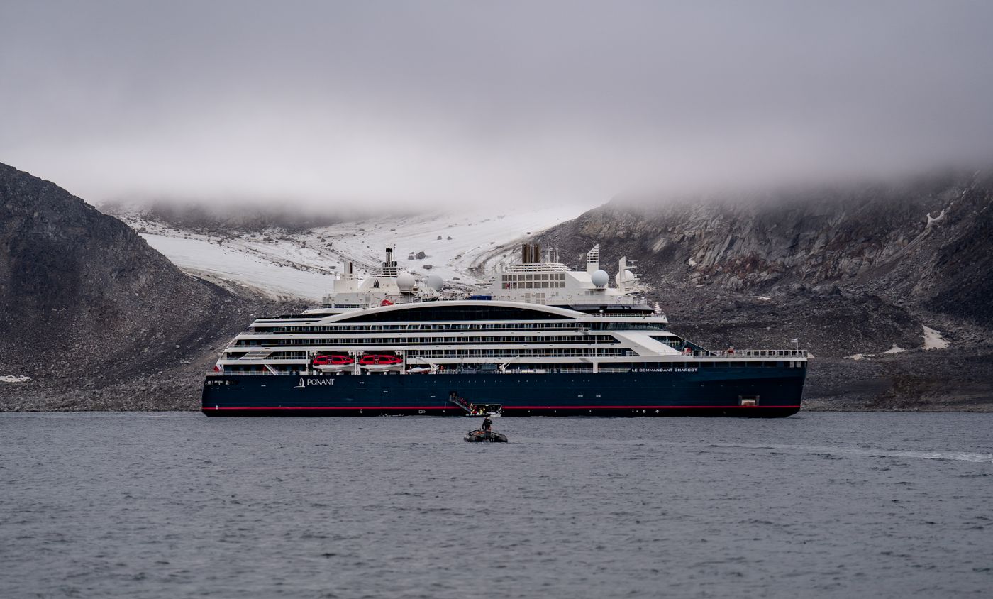 A luxury expedition ship moving through fog between rugged hills on the Norwegian coast