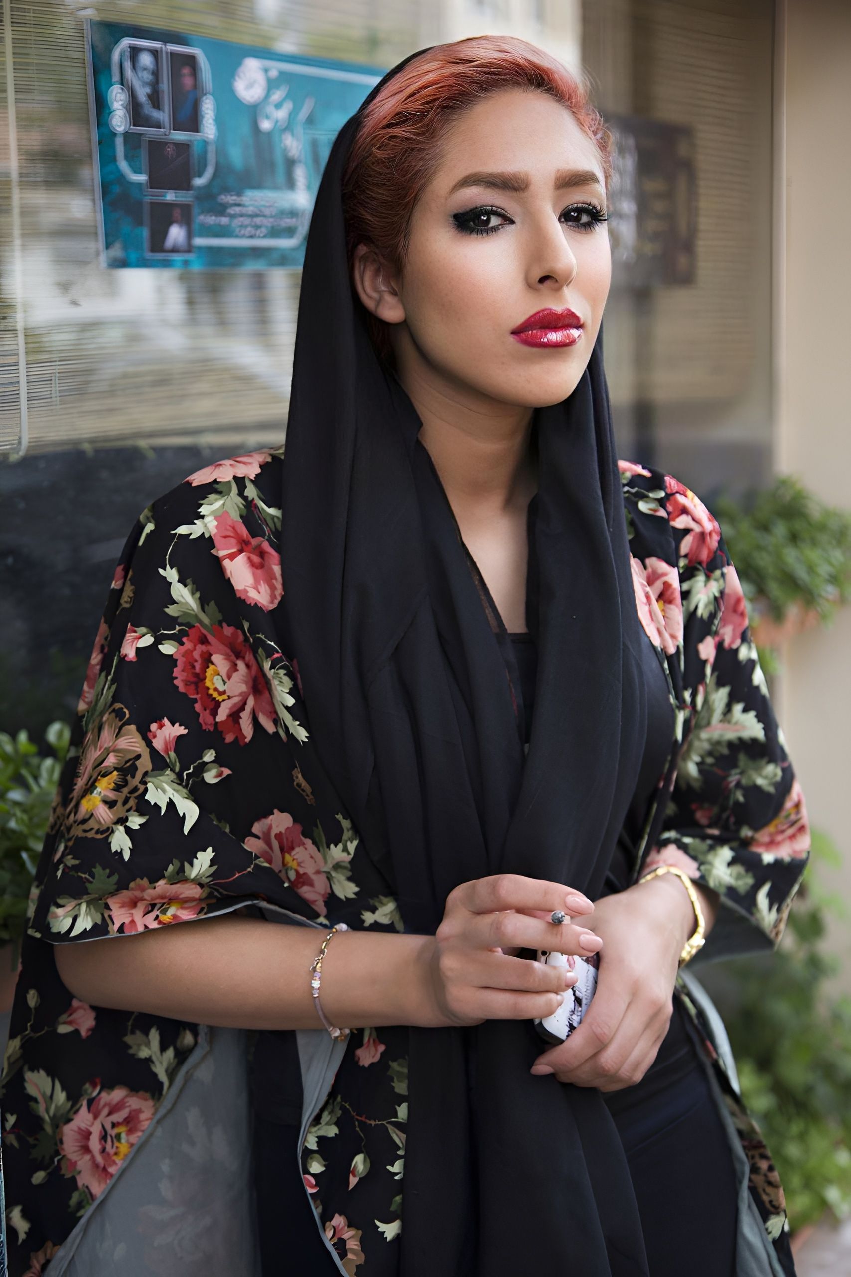 Elegant woman in floral attire with headscarf, standing outdoors, exuding confidence.