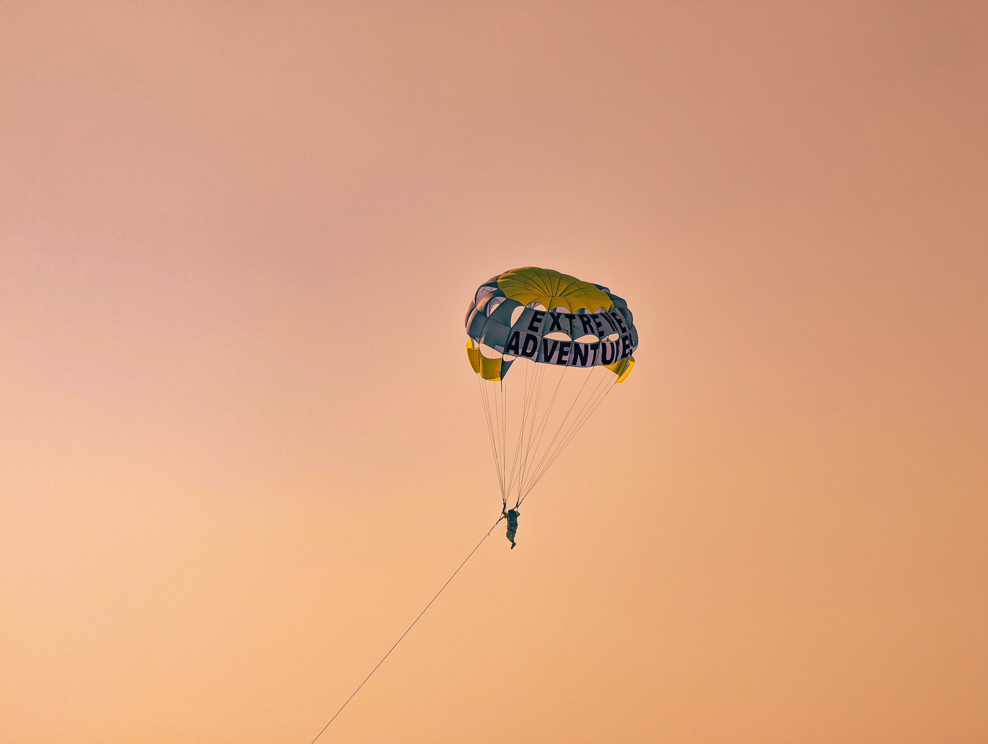 Silhouette of a person parasailing against a rich orange sunset sky, embodying adventure.