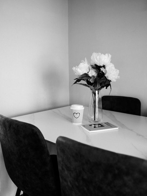 Free Elegant black and white photo of a minimalist dining area featuring a vase of white flowers on a table. Stock Photo