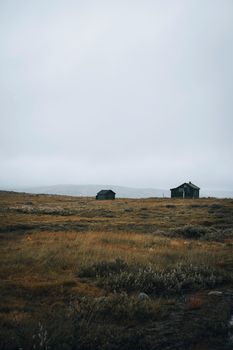 Two isolated cabins stand in a foggy, grassy landscape, offering a sense of solitude and serenity.