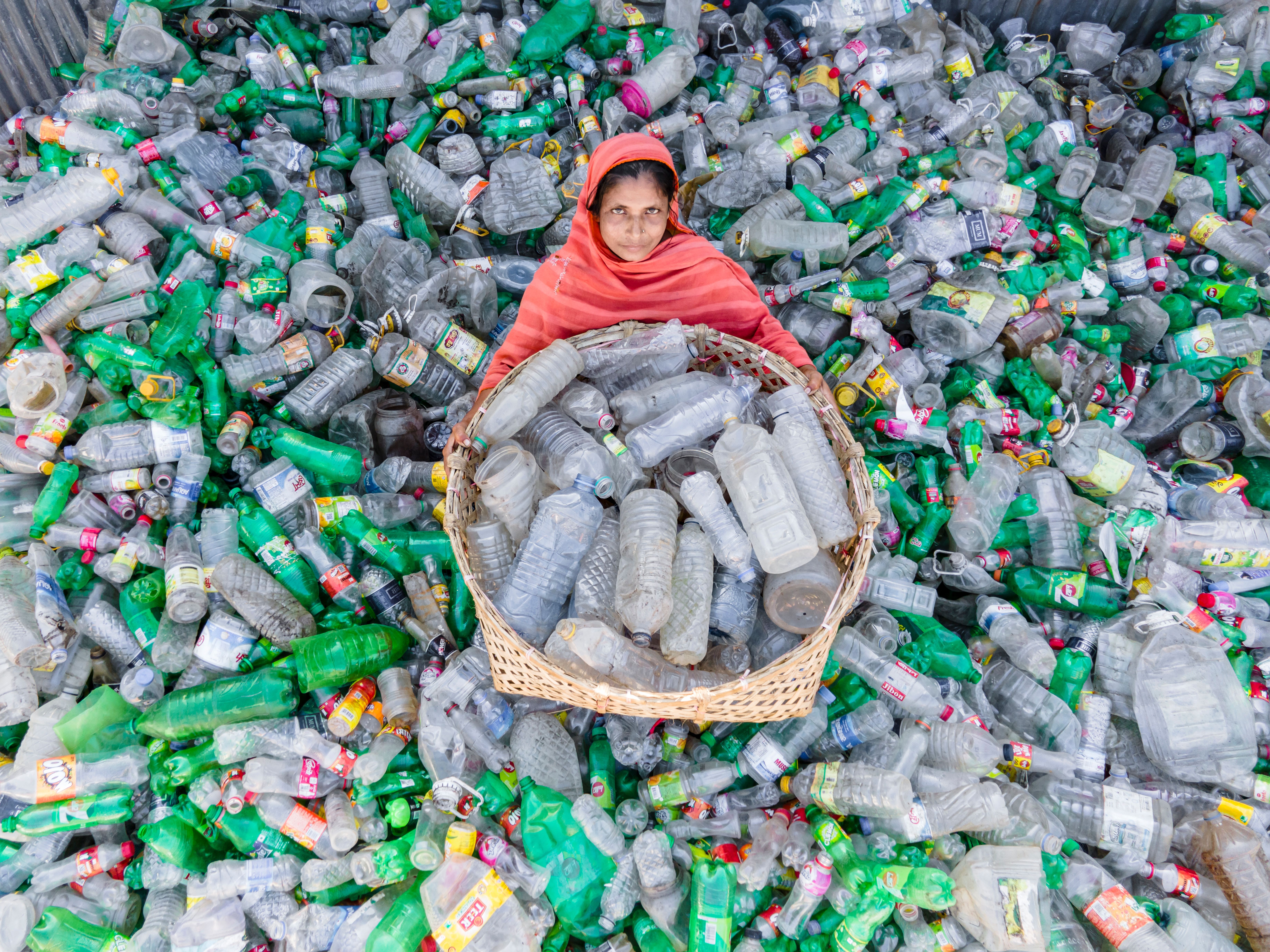 A woman in vibrant attire collects plastic bottles for recycling to promote environmental sustainability. - Common Misconceptions About Eco-Friendly Handbags