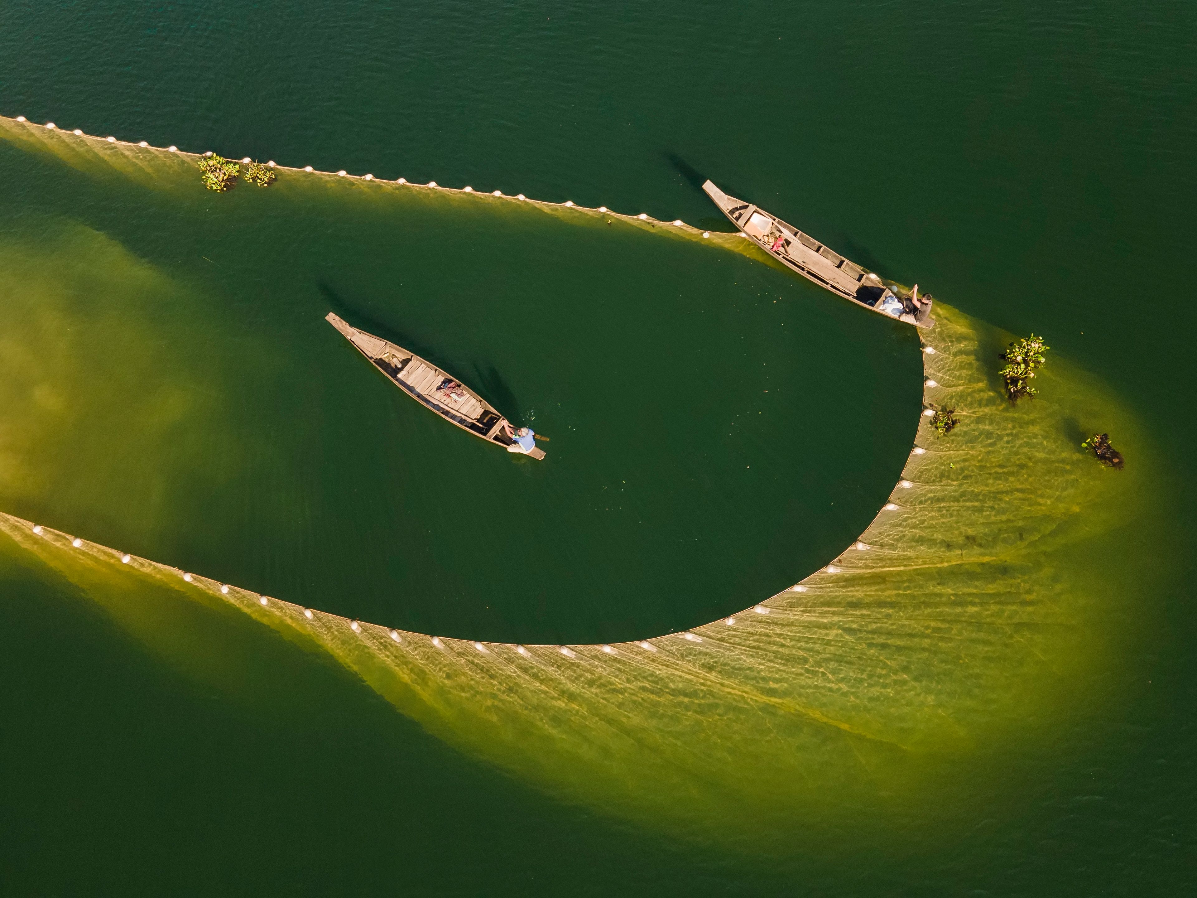 Aerial view of two fishing boats and nets on a vibrant green river, creating an artistic pattern.