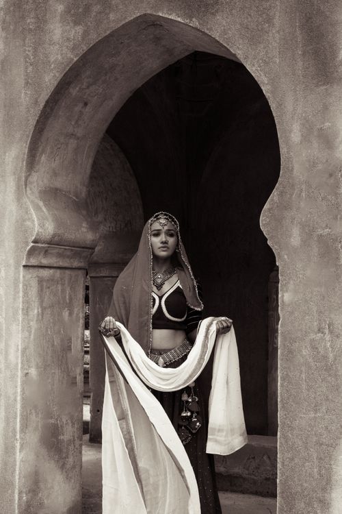 Free Woman in traditional dress standing in an ornate historic archway, sepia tone. Stock Photo
