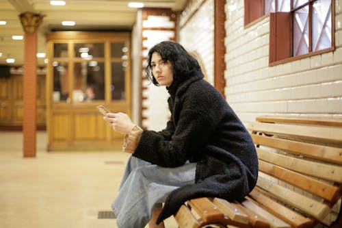 Woman in Black Sweater Sitting on Brown Wooden Bench