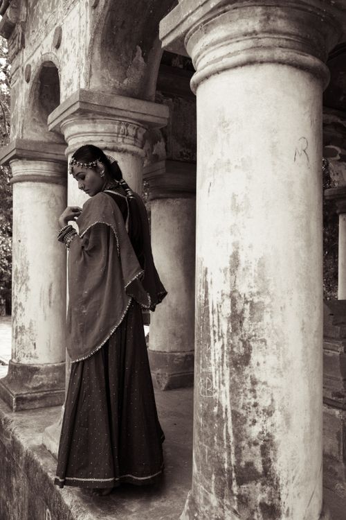 Free Sepia-toned image of a woman in traditional attire beside ancient columns. Stock Photo