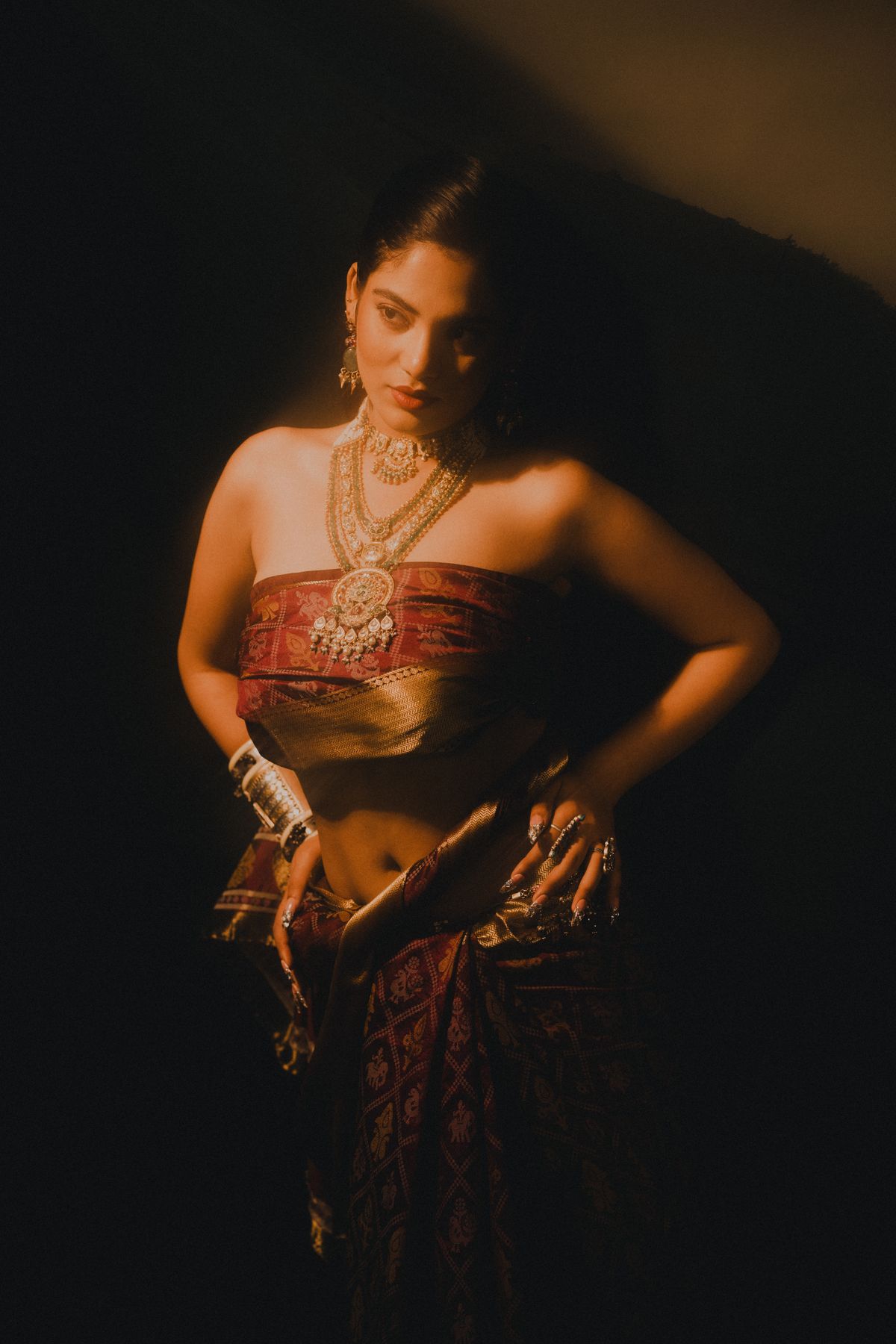 Woman in a traditional saree and jewellery lit by warm lamplight