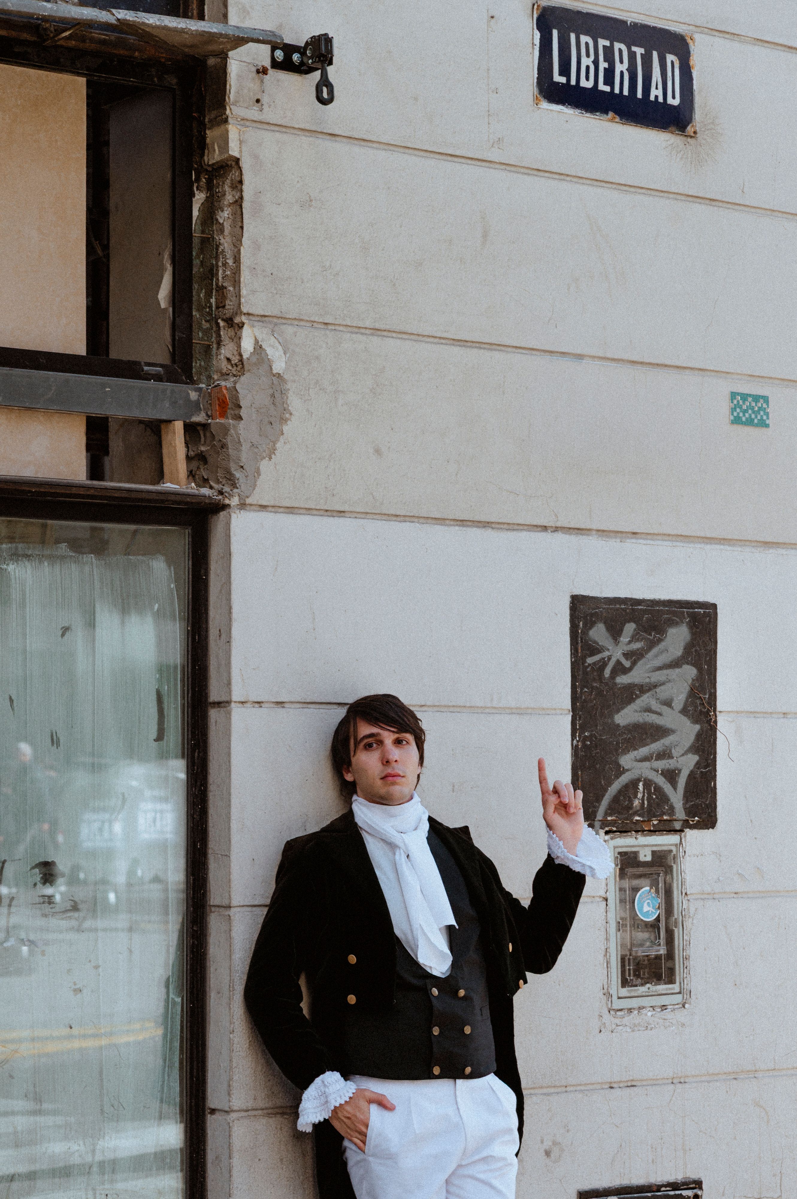 A man in period clothing stands outdoors, gesturing towards a 'Libertad' street sign.