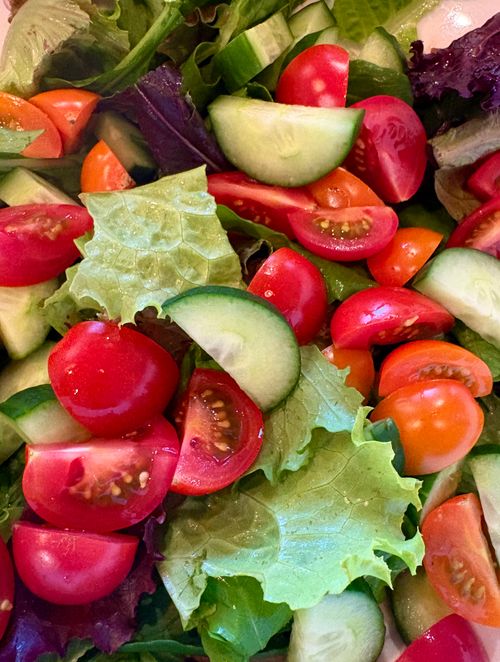 Free Vibrant close-up of a fresh tomato and cucumber salad with mixed greens. Stock Photo