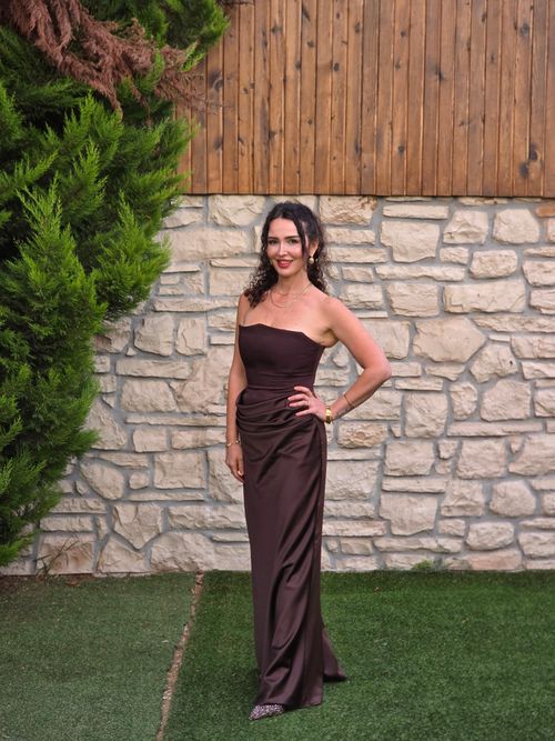 Free Woman wearing a brown gown poses against a stone wall outdoors. Stock Photo