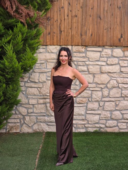 Free Portrait of a woman in a brown evening gown standing against a stone wall outdoors. Stock Photo
