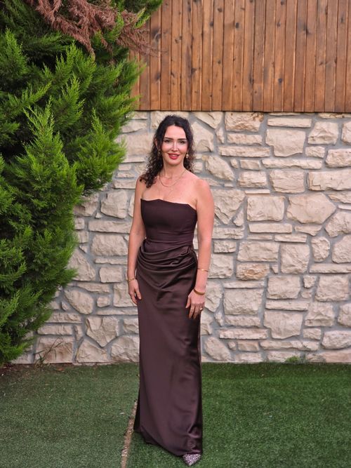 Free A woman in a brown gown stands elegantly by a stone wall, outdoors. Stock Photo
