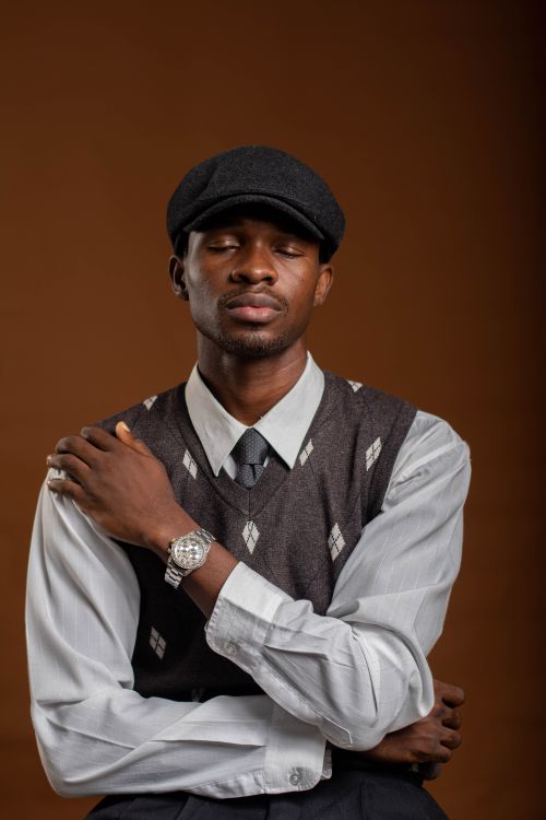 Free Portrait of a fashionable man wearing a sweater vest and cap against a brown background. Stock Photo