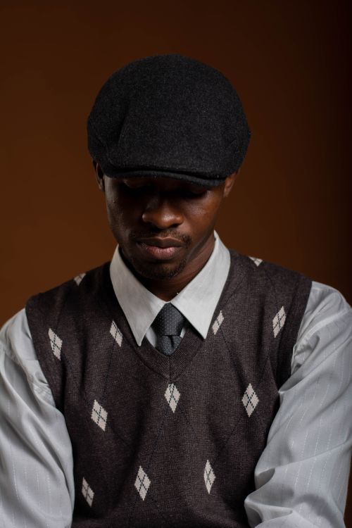 Free Portrait of a thoughtful man wearing a flat cap and sweater vest under warm lighting. Stock Photo