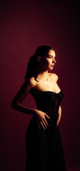 A fashionable woman poses dramatically in a sleek black dress with a moody backdrop.
