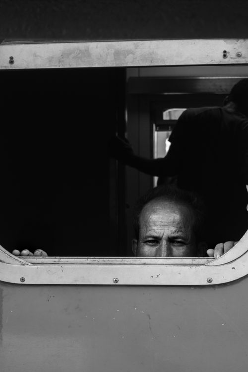 Free A black and white image of a man peering through a train window, captured candidly. Stock Photo