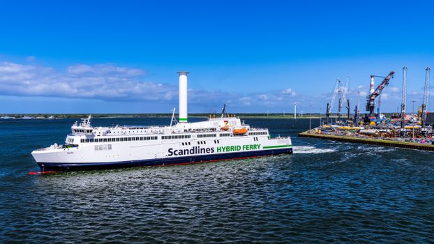 Scandlines hybrid ferry navigating through Rostock harbor under a clear blue sky with industrial backdrop.