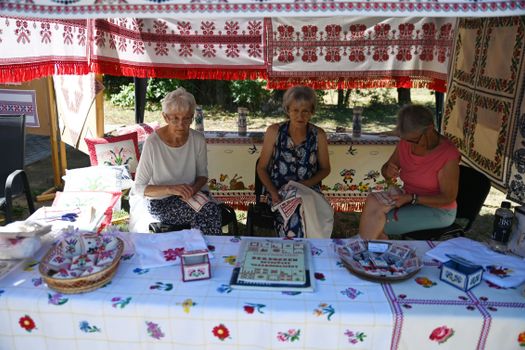 Three women showcasing handmade embroidery at a vibrant outdoor market stall.