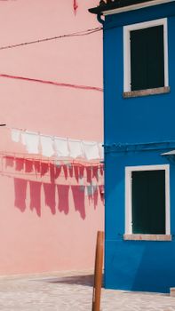 Colorful facade in Burano, Italy, with hanging laundry casting shadows.