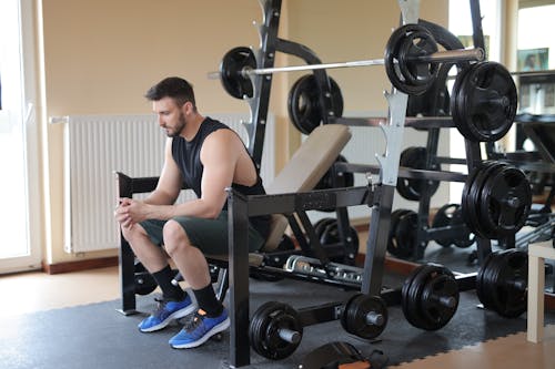 Man in Black Tank Top and Blue Nike Shoes Sitting on Bench Press