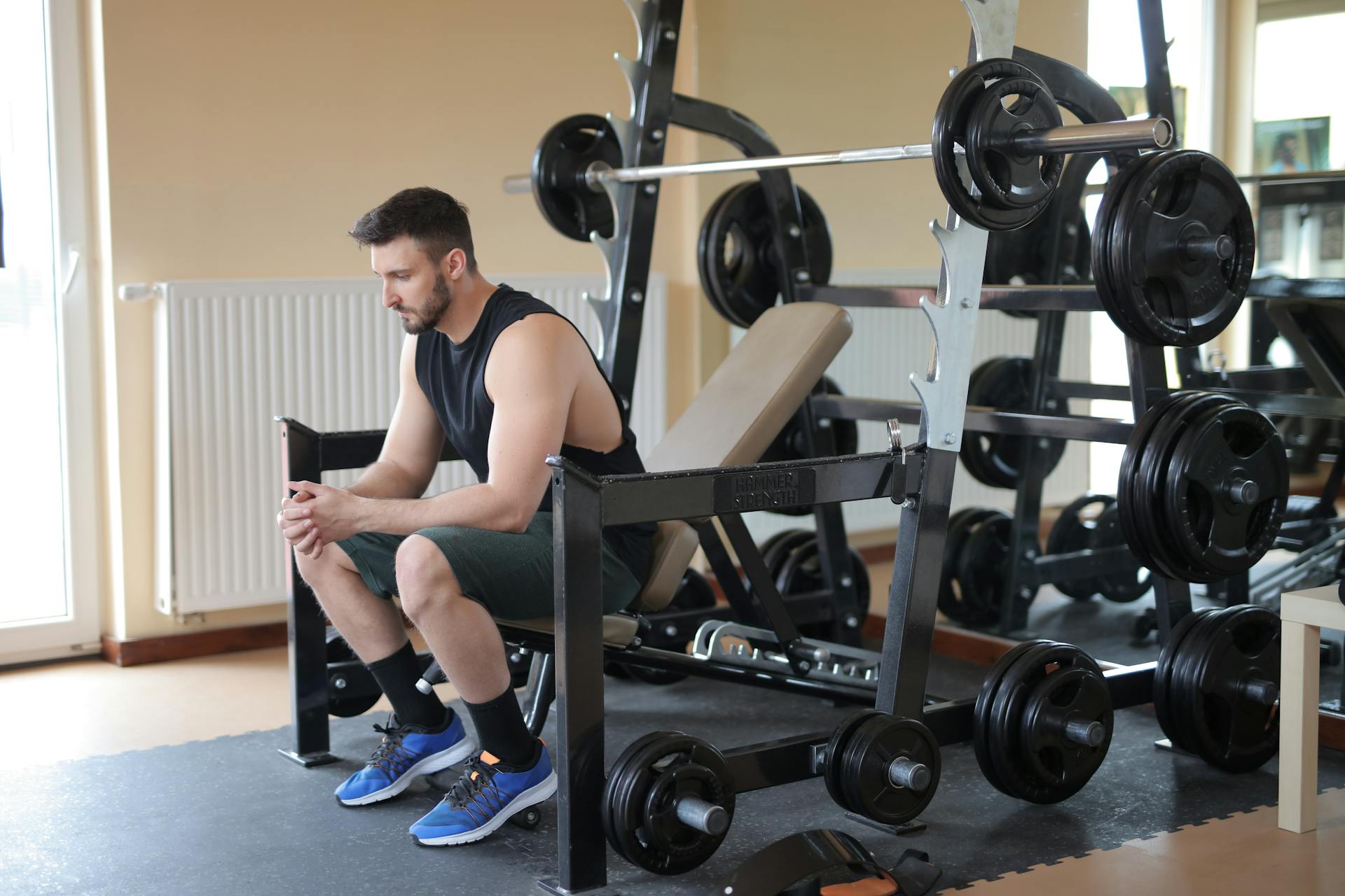 Man in Black Tank Top and Blue Nike Shoes Sitting on Bench Press