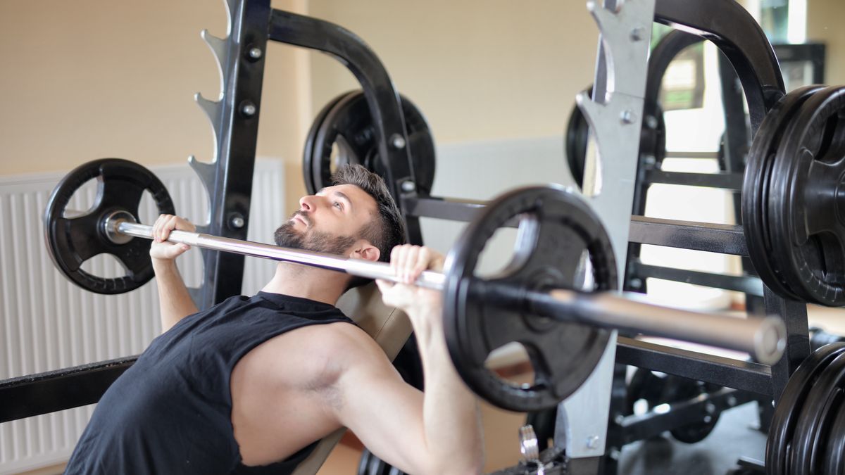 Adult man performing a bench press exercise at the gym, focusing on strength and muscle building.