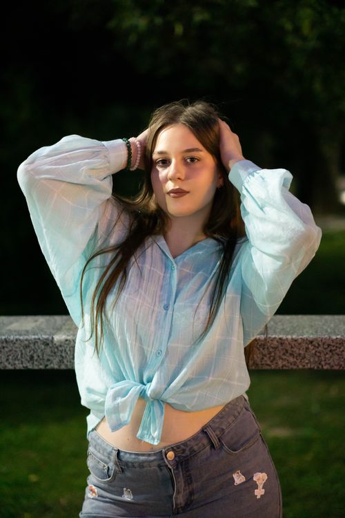 Free Casual portrait of a young woman wearing a blue blouse and denim jeans, posing outdoors at night. Stock Photo