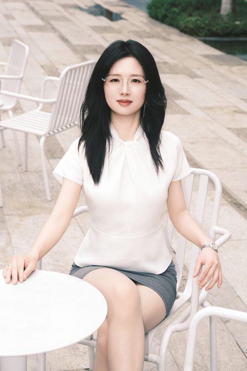Free Stylish woman sitting at a cafe in Xi'an with a confident gaze wearing a white blouse and gray skirt. Stock Photo