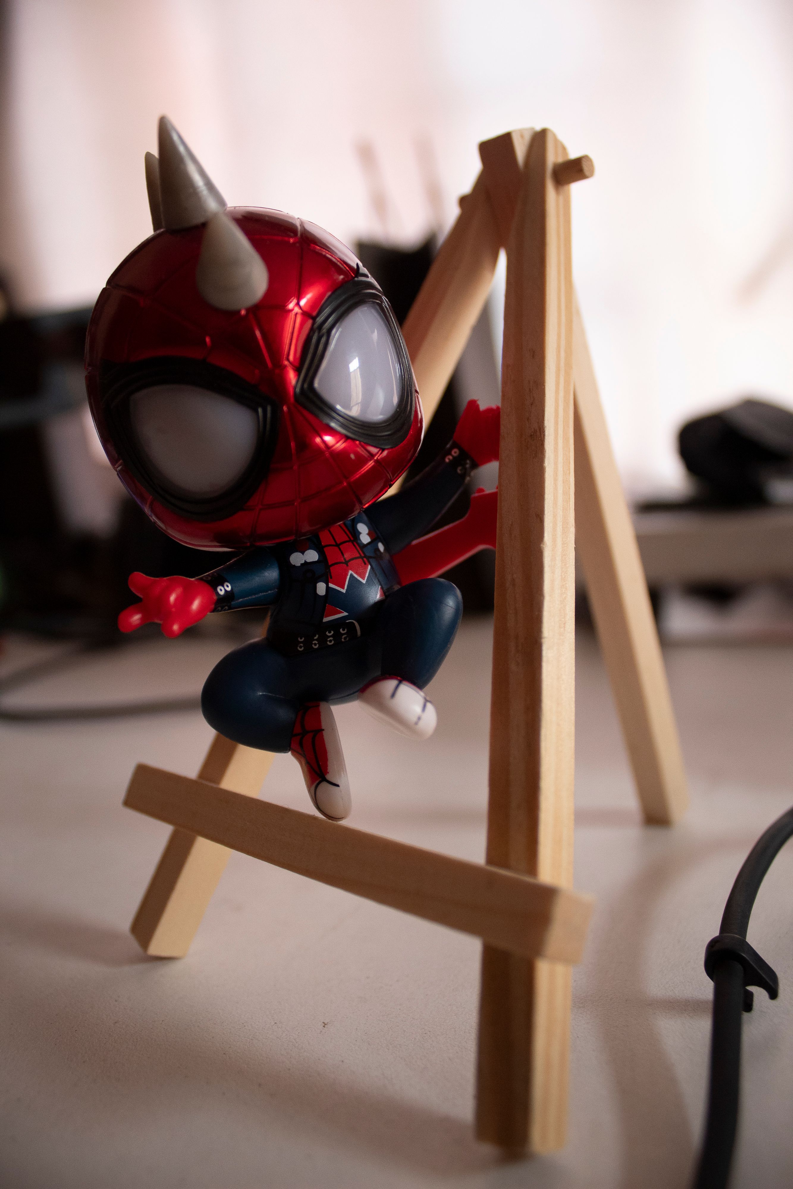 Close-up of a superhero action figure climbing a wooden easel inside a room.