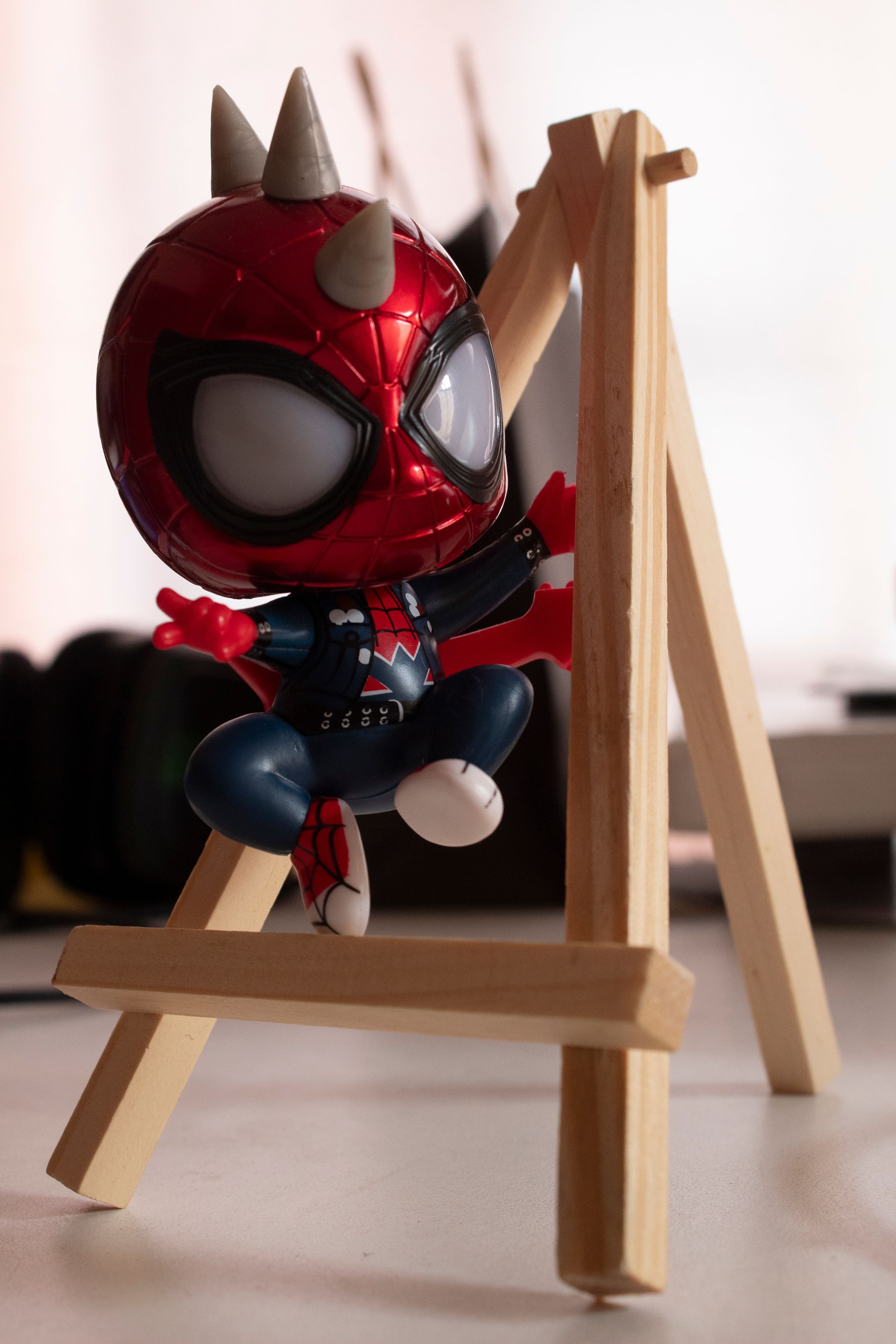 Close-up of a mini superhero figurine in vibrant red and blue on a wooden easel indoors.