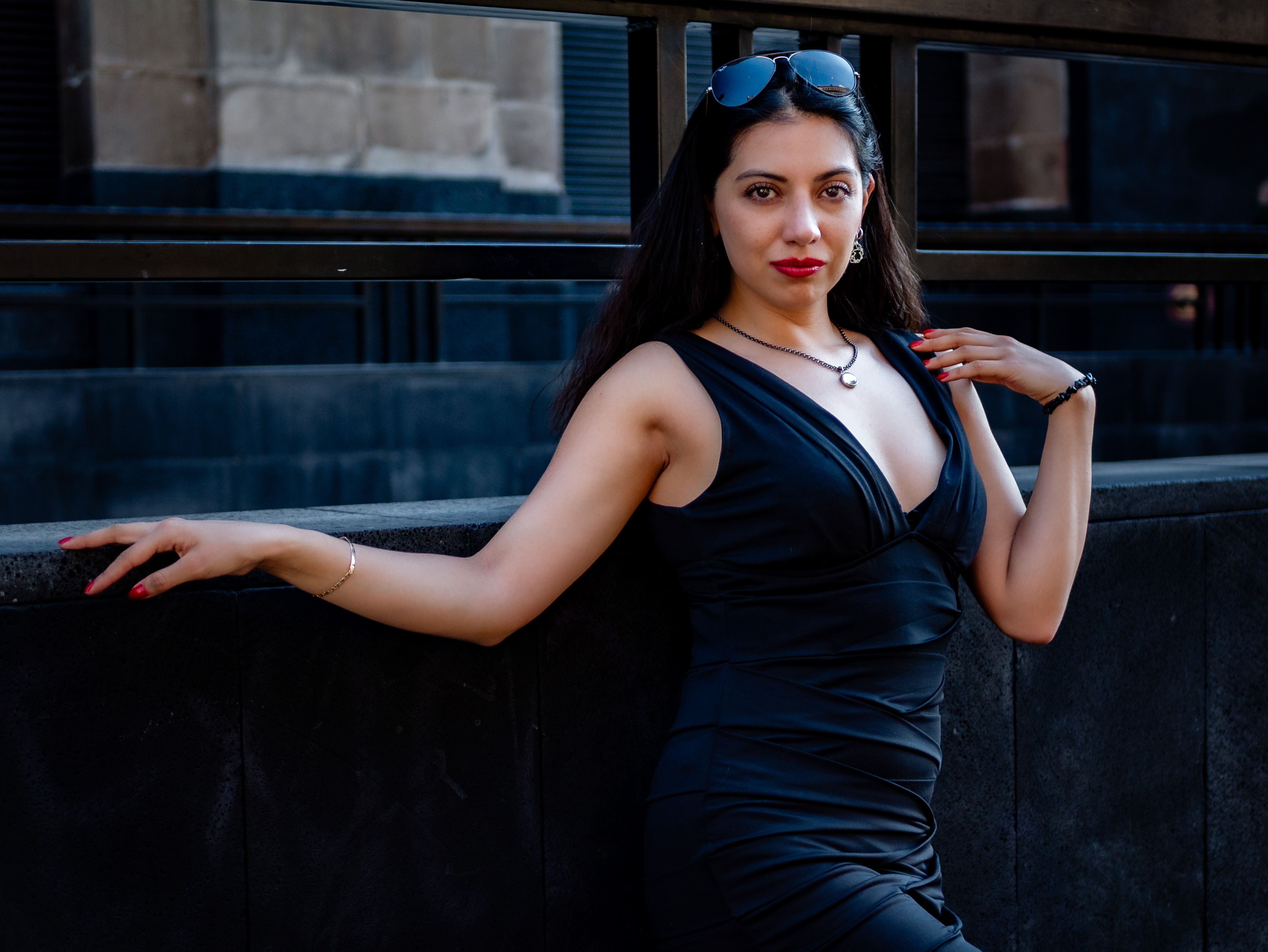 Stylish woman in black dress posing against urban backdrop, exuding confidence and elegance.