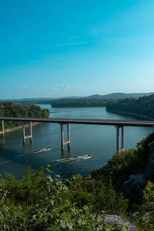 Free Stunning view of a bridge crossing a river with boats below amid lush greenery. Stock Photo